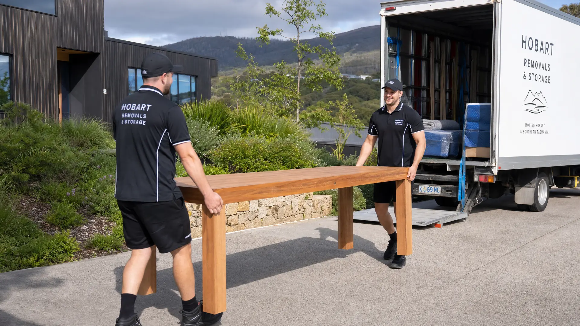 Two Hobart removalists carrying a solid timber dining table to a moving truck